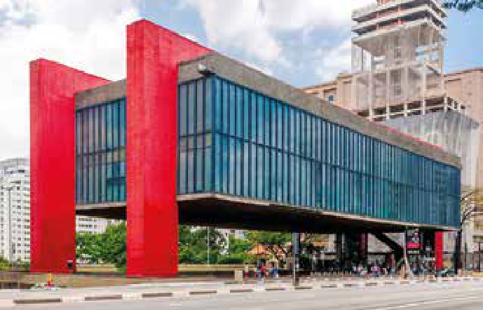 Fotografia do edifício do Museu de Arte de São Paulo, com grandes pilares vermelhos, bloco elevado envidraçado e vão livre abaixo.