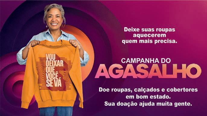 Cartaz da campanha do agasalho com uma mulher segurando uma blusa e informações que solicitam roupas, calçados e cobertores em bom estado.