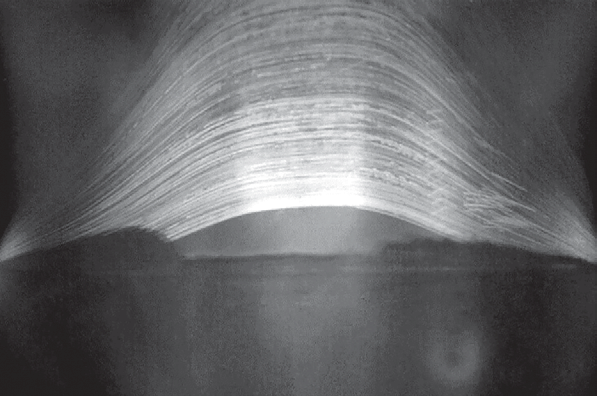 Fotografia em preto e branco com numerosos arcos luminosos cruzando o céu, produzidos pelo percurso aparente do Sol durante uma longa exposição.