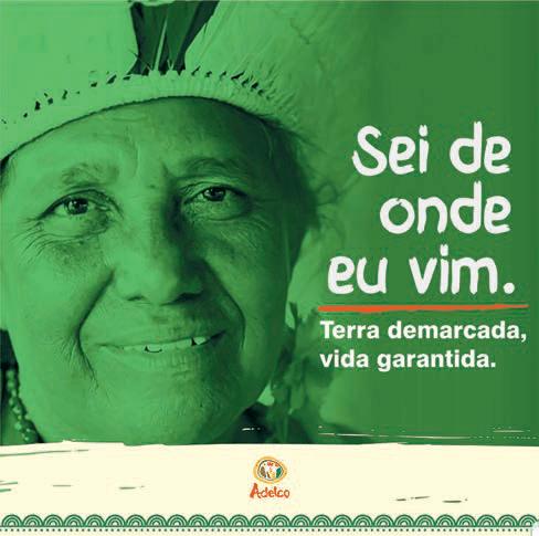 Cartaz verde com fotografia de uma pessoa usando cocar e os dizeres Sei de onde eu vim. Terra demarcada, vida garantida. Na parte inferior aparece a marca Adelco.