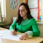a woman in green long sleeve shirt sitting at the table holding a pencil on paper